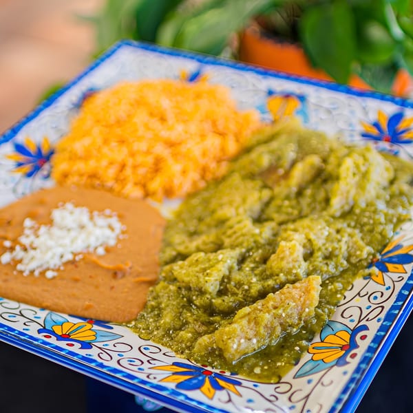 A colorful plate of El Arriero Taqueria's green chile pork, refried beans, and Mexican rice.