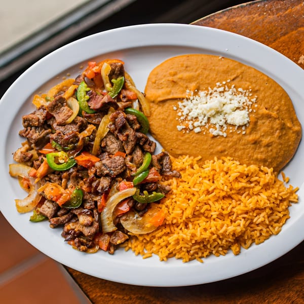 El Arriero Taqueria's carne asada with onions, peppers, rice, and refried beans on a white plate.