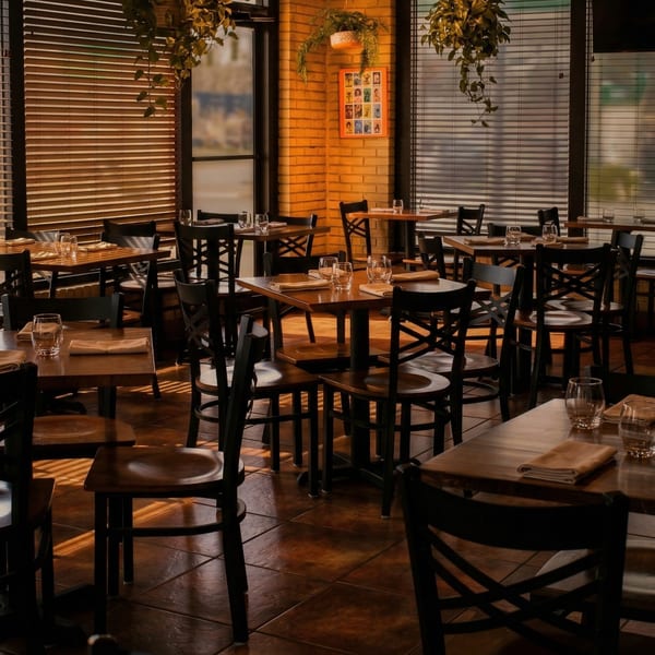 Warmly lit El Arriero Taqueria dining room with wooden tables, chairs, and window blinds.