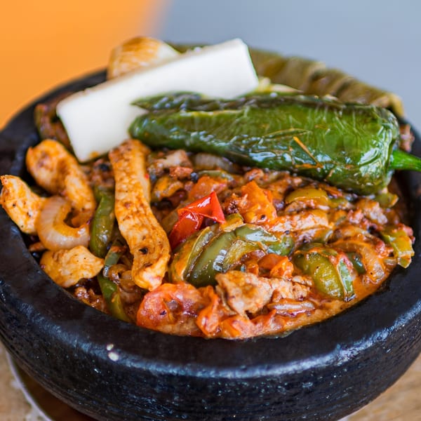 El Arriero Taqueria's sizzling molcajete with chicken, peppers, onions, and cheese in a black bowl.