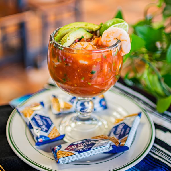 Shrimp cocktail with avocado, lime, and crackers on a white plate at El Arriero Taqueria.