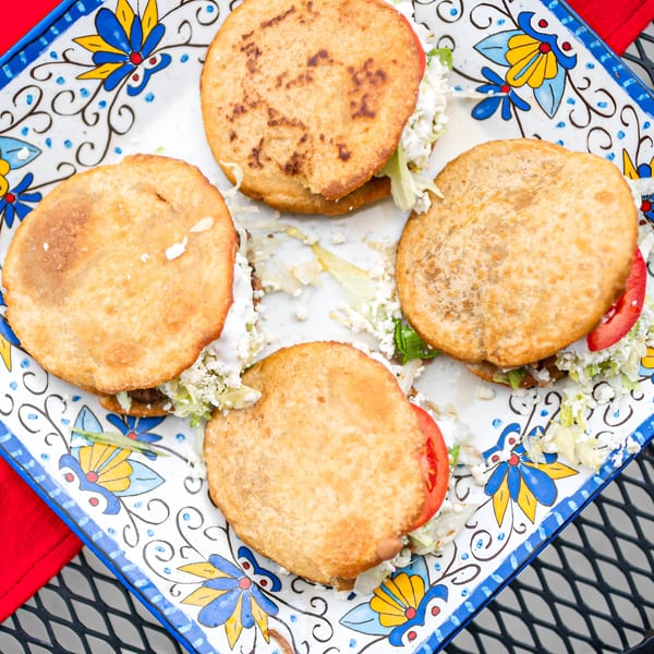 Four El Arriero sopes with lettuce, cheese, and tomato on a decorative white and blue plate.