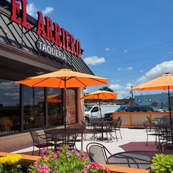 El Arriero Taqueria's outdoor patio with orange umbrellas, black tables, and chairs under a blue sky.