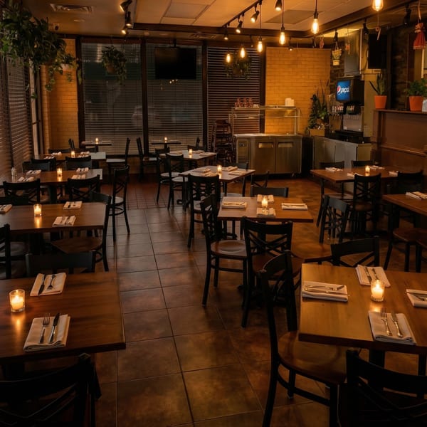 Warmly lit El Arriero Taqueria dining room with many empty tables set with candles and silverware.
